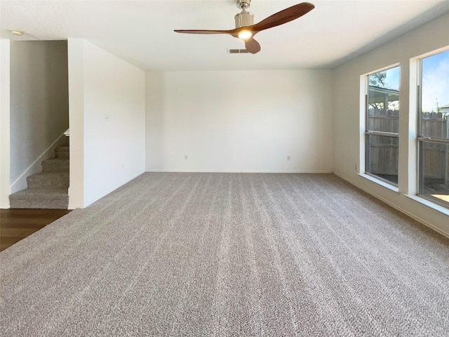 spare room featuring carpet floors, ceiling fan, baseboards, and stairs