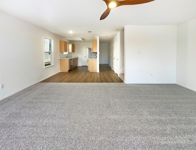 unfurnished living room with carpet flooring, a sink, a ceiling fan, and baseboards