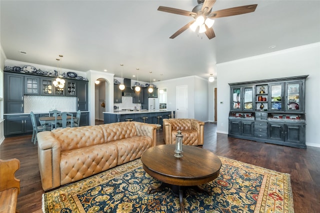 living room featuring baseboards, ornamental molding, dark wood finished floors, and ceiling fan with notable chandelier