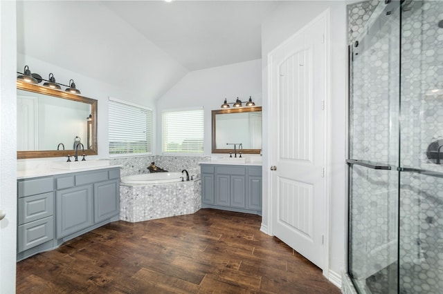 full bath featuring wood finished floors, two vanities, a stall shower, a garden tub, and lofted ceiling