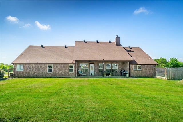 rear view of property featuring a chimney, brick siding, fence, and a yard