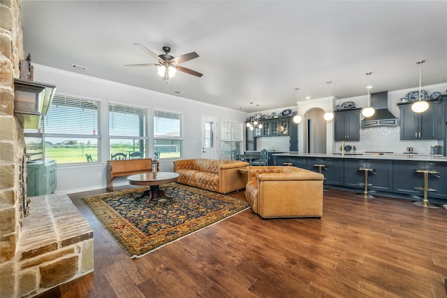 living area with dark wood-style floors, ceiling fan, crown molding, visible vents, and baseboards