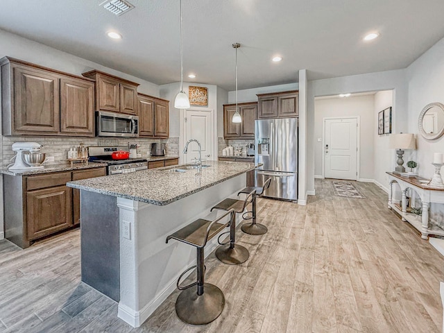 1005 Napier Way, Fort Worth, TX 76247 - kitchen featuring appliances with stainless steel finishes, a sink, light stone countertops, tasteful backsplash, and a kitchen breakfast bar