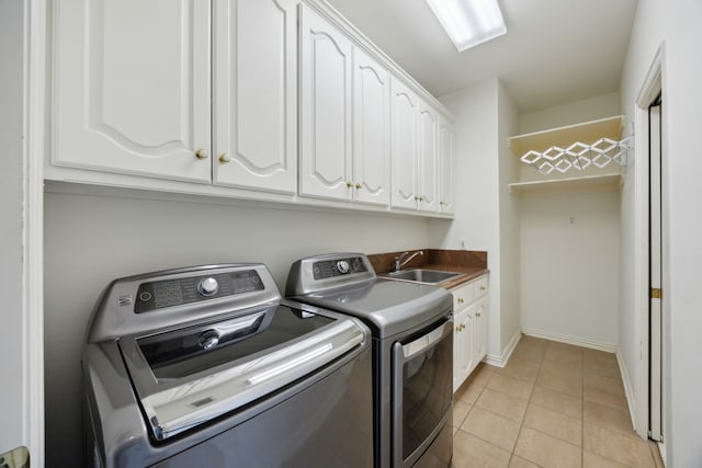 laundry area with baseboards, light tile patterned flooring, washer and clothes dryer, cabinet space, and a sink