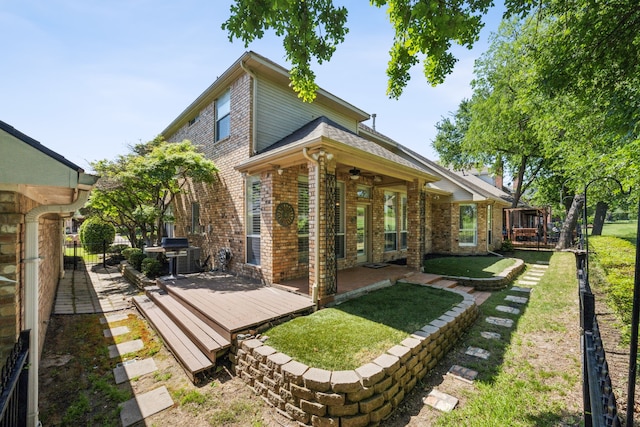 back of house featuring a wooden deck, a yard, a ceiling fan, fence, and brick siding