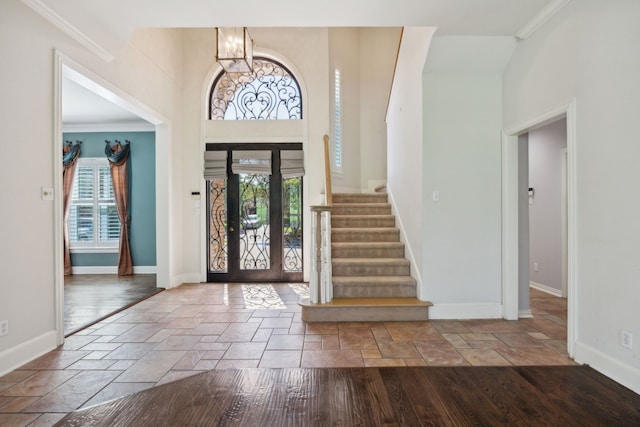 foyer entrance featuring ornamental molding, stairway, baseboards, stone tile flooring, and a notable chandelier