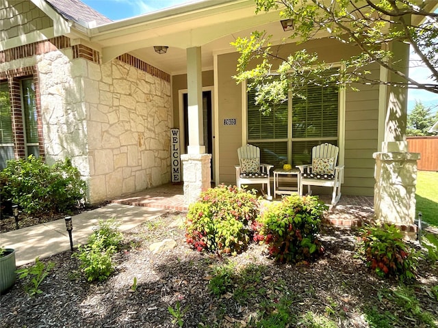 view of exterior entry with stone siding, a shingled roof, and covered porch