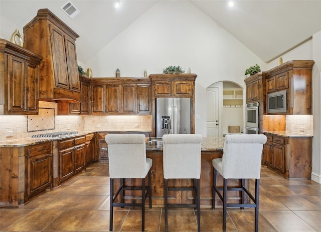 1011 Caribou Dr, Prosper, TX 75078 - kitchen featuring appliances with stainless steel finishes, high vaulted ceiling, a kitchen island, arched walkways, and backsplash