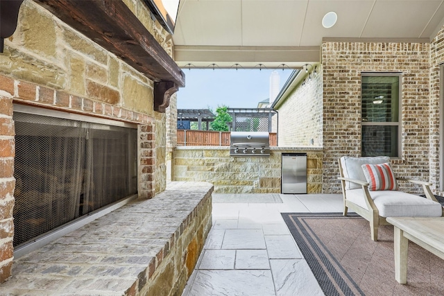 view of patio / terrace featuring exterior kitchen, an outdoor brick fireplace, and a grill