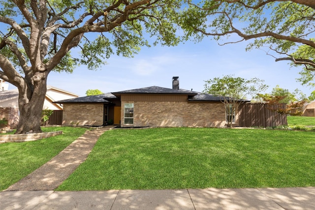 view of front facade with a front yard, fence, brick siding, and a chimney