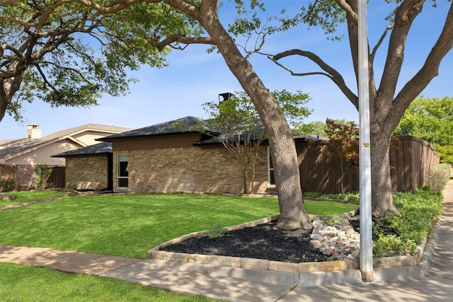 view of front of property featuring a front yard, brick siding, fence, and a chimney
