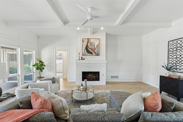 living room with light wood-style floors, a decorative wall, visible vents, and beamed ceiling
