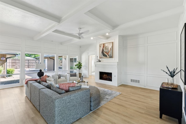 living room featuring a decorative wall, beamed ceiling, light wood-type flooring, a warm lit fireplace, and visible vents
