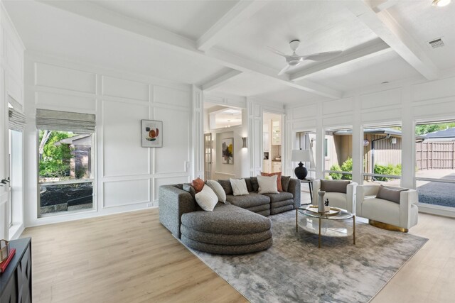 living room featuring a decorative wall, beam ceiling, a ceiling fan, and visible vents