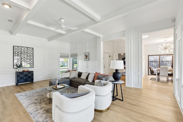 living room with visible vents, a decorative wall, light wood-type flooring, beam ceiling, and ceiling fan with notable chandelier