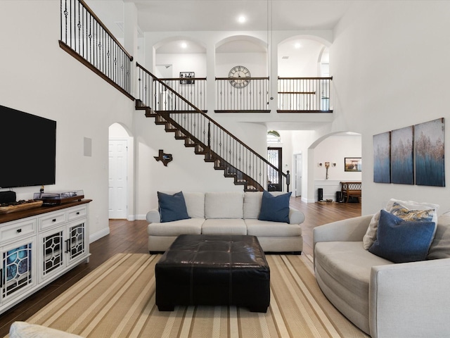 living area featuring arched walkways, a high ceiling, wood finished floors, and stairway