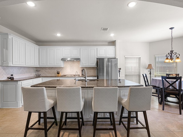 kitchen with appliances with stainless steel finishes, under cabinet range hood, visible vents, decorative backsplash, and a sink