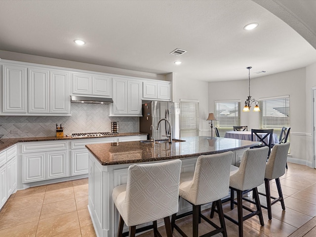kitchen with backsplash, a center island with sink, visible vents, stainless steel appliances, and a sink