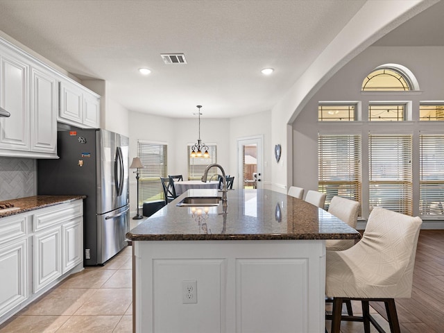 kitchen with white cabinetry, freestanding refrigerator, visible vents, a kitchen bar, and a sink