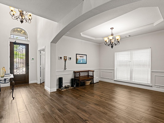 entrance foyer with visible vents, arched walkways, an inviting chandelier, a tray ceiling, and wood finished floors