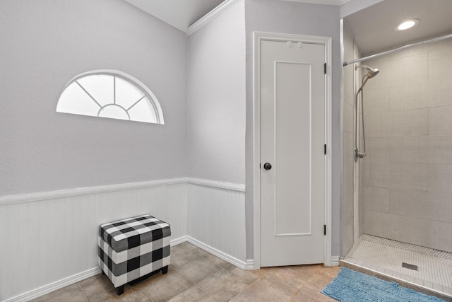 bathroom featuring crown molding, tile patterned floors, a wainscoted wall, and a tile shower