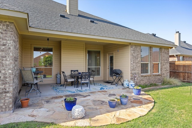 back of property with a chimney, fence, a patio, brick siding, and roof with shingles