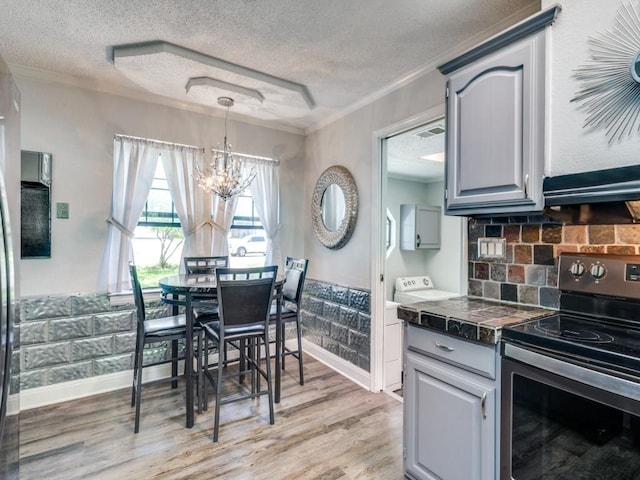 kitchen featuring stainless steel electric range, light wood-style floors, a textured ceiling, and an inviting chandelier