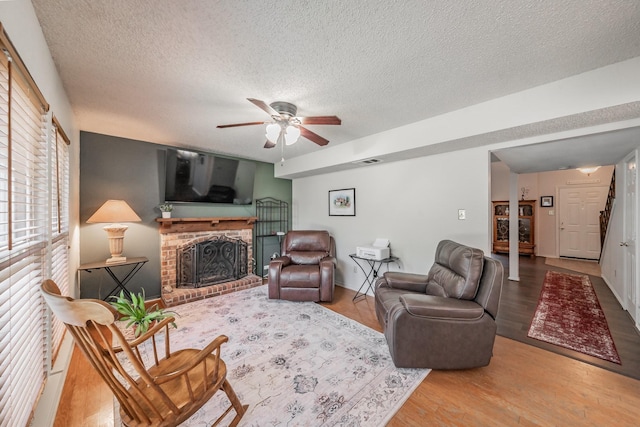 living room with a brick fireplace, a ceiling fan, wood finished floors, and a textured ceiling