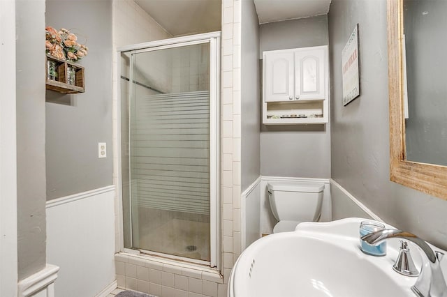 bathroom featuring a shower stall, toilet, a wainscoted wall, and a sink