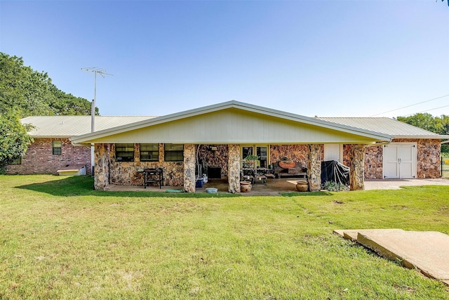 back of house with a lawn, stone siding, a patio area, and metal roof