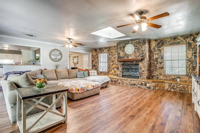 living room with ceiling fan, a fireplace, visible vents, a skylight, and hardwood / wood-style flooring