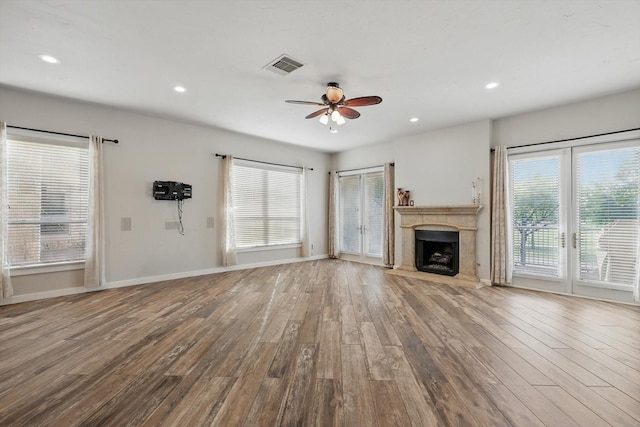 unfurnished living room with visible vents, a premium fireplace, a ceiling fan, and wood finished floors