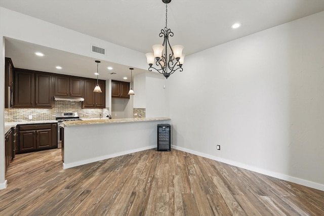 kitchen featuring stainless steel gas stove, dark brown cabinetry, visible vents, under cabinet range hood, and wood finished floors