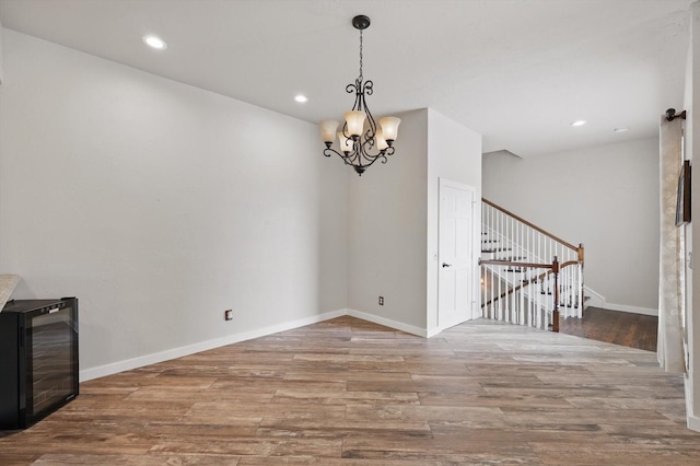 unfurnished dining area with baseboards, a chandelier, stairway, wine cooler, and wood finished floors