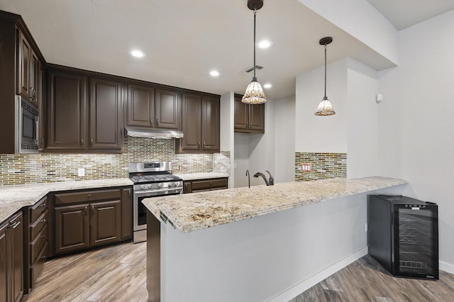 kitchen featuring light wood-type flooring, dark brown cabinetry, under cabinet range hood, wine cooler, and stainless steel appliances