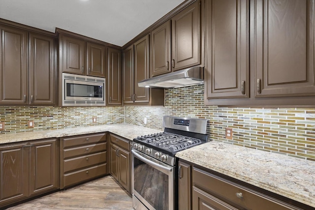 kitchen featuring under cabinet range hood, dark brown cabinets, backsplash, and stainless steel appliances
