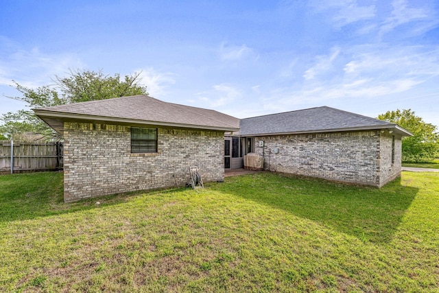 back of property featuring brick siding, fence, a shingled roof, and a lawn