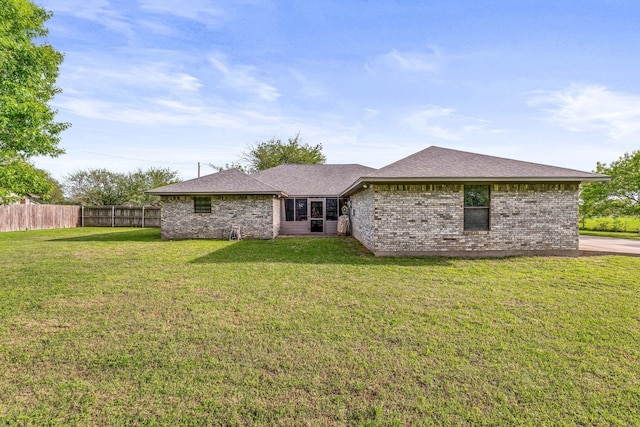 rear view of property with roof with shingles, brick siding, fence, and a lawn