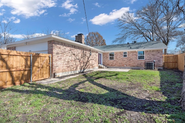 back of property with a yard, a fenced backyard, brick siding, a gate, and a chimney