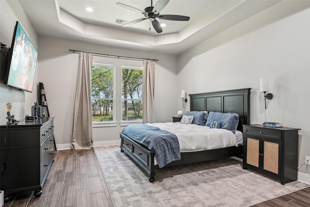 bedroom with visible vents, baseboards, a ceiling fan, a tray ceiling, and wood finish floors