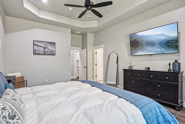 bedroom with dark wood-style flooring, baseboards, a raised ceiling, and a ceiling fan
