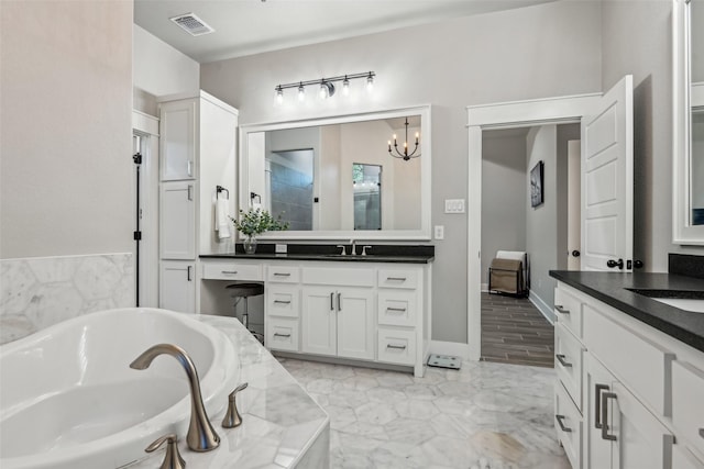 full bathroom featuring two vanities, a bath, visible vents, a chandelier, and a sink