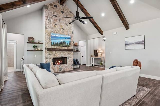 living room featuring ceiling fan, beamed ceiling, a stone fireplace, baseboards, and dark wood-style floors