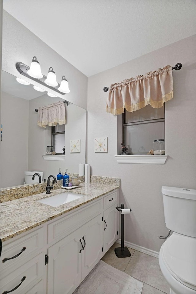 bathroom featuring tile patterned flooring, vanity, baseboards, and toilet