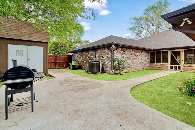 rear view of house featuring central AC, fence, a patio, brick siding, and roof with shingles