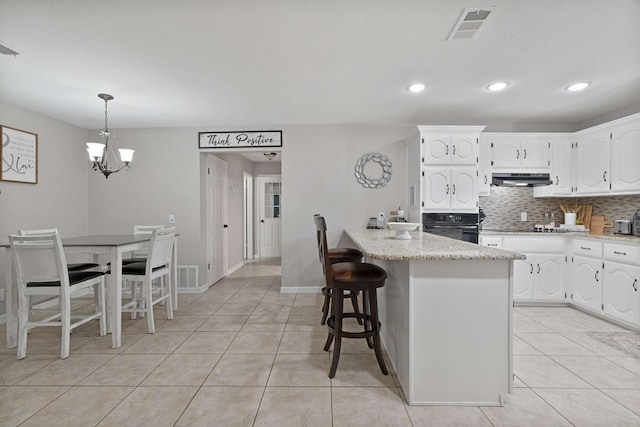 kitchen with light tile patterned floors, white cabinetry, a kitchen breakfast bar, and black oven