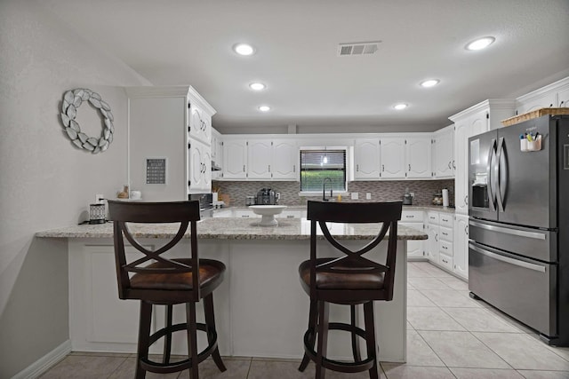kitchen featuring a peninsula, white cabinets, a breakfast bar, light stone counters, and stainless steel fridge