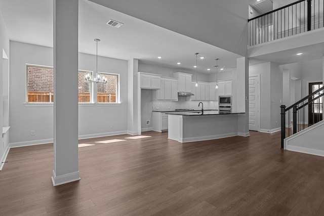 unfurnished living room with dark wood-type flooring, visible vents, baseboards, and stairs