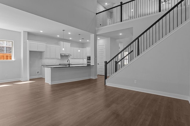 unfurnished living room with baseboards, recessed lighting, stairs, dark wood finished floors, and a sink