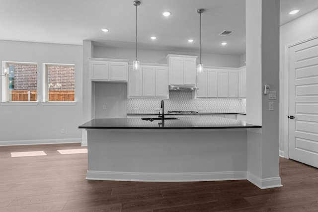 kitchen with a sink, backsplash, dark countertops, and white cabinetry
